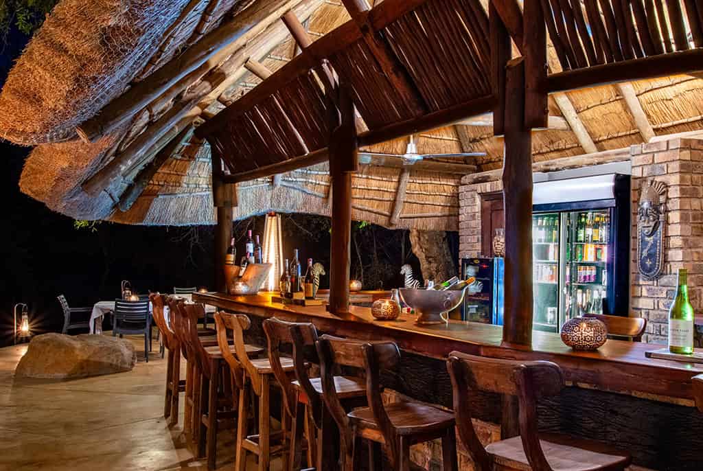 Luxurious bar area inside Idube Game Reserve lodge with rustic wooden furniture, thatched roof, and cozy ambiance, perfect for a safari experience.
