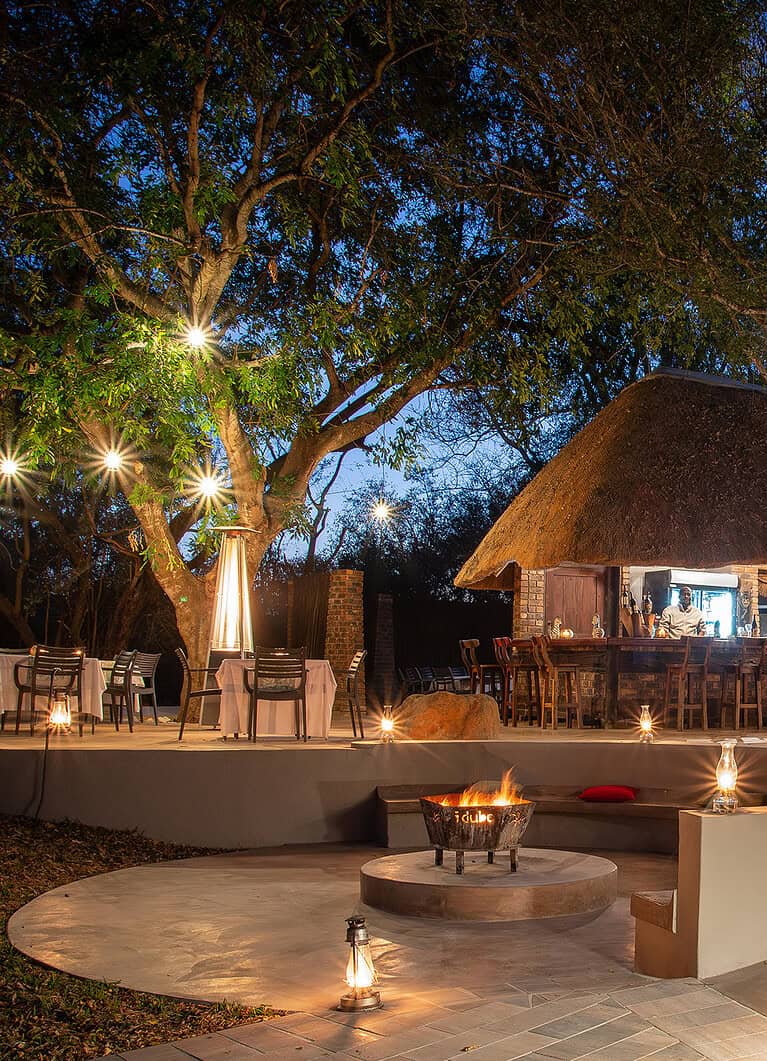 Luxurious outdoor lounge at Idube Game Reserve, surrounded by lush trees and authentic thatched-roof structures, offering an immersive safari experience in South Africa.